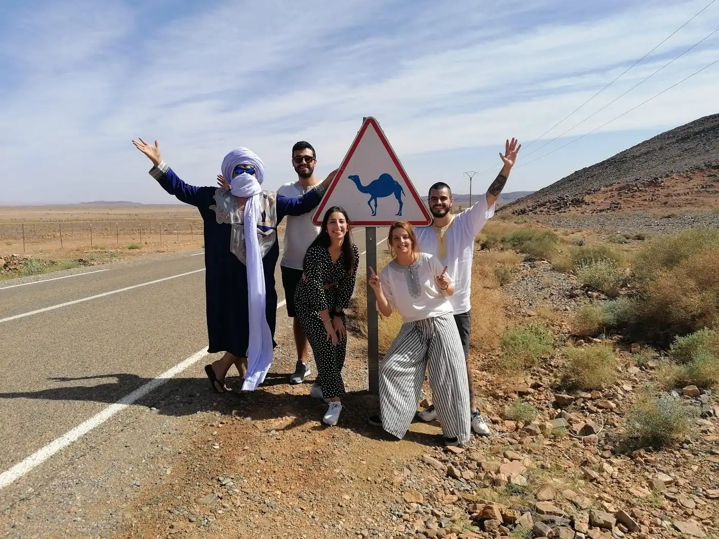 A Morocco Tours driver and guide with travelers beside a vehicle on an Atlas mountain road