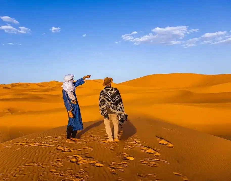A Morocco Tours guide pointing across the sand dunes of Erg Chebbi near Merzouga with a traveler